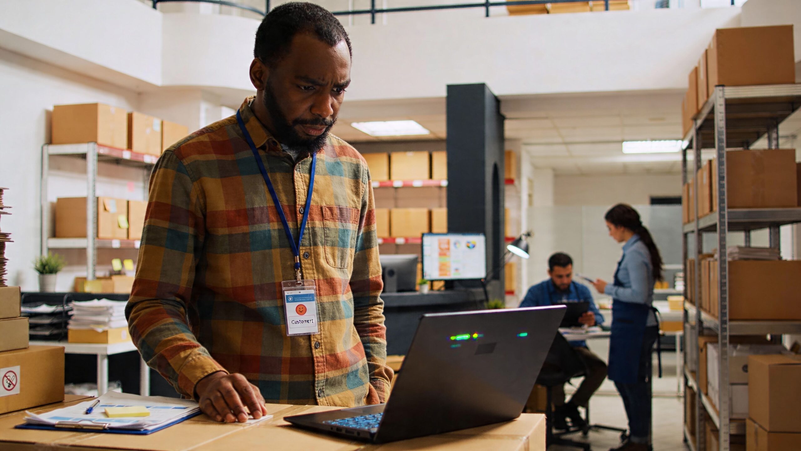 A professional warehouse worker with a badge using a laptop to organize inventory for shipping logistics.